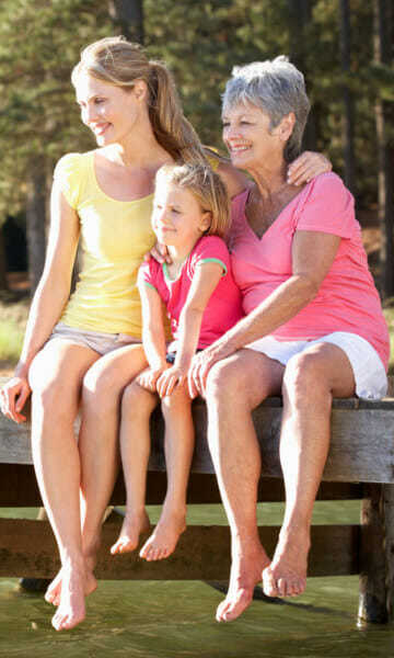 Grandma, Mum and Daughter sitting on a pier swinging their bare legs and ankles over the edge.